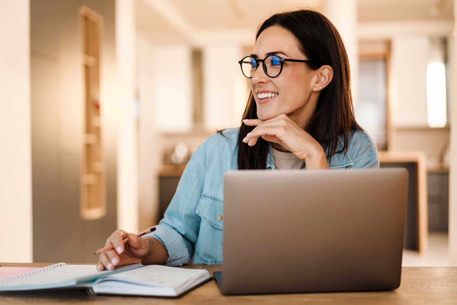 Smiling woman on laptop taking notes at her desk